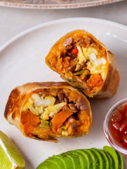 Toasted breakfast burrito halves served with sliced avocado and salsa.