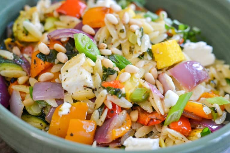 Close-up of lemon orzo with roasted vegetables, fresh basil, and chunks of feta cheese
