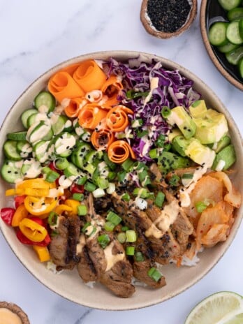 Beef bulgogi bowls with thin strips of marinated and grilled ribeye, rice, carrots, cabbage, avocado, kimchi, cucumbers, bell peppers, green onions and sriracha mayo