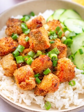 Crispy nuggets of salmon sit on top of white rice with some green onions and sliced cucumbers