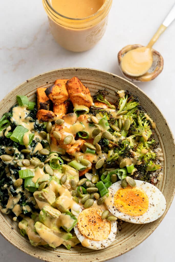 Bowl with quinoa, broccoli, sweet potato, kale, hard boiled egg and spicy cashew dressing on top