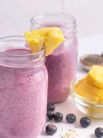 Blueberry pineapple smoothie in 2 jars with chia seeds and pineapple on the side