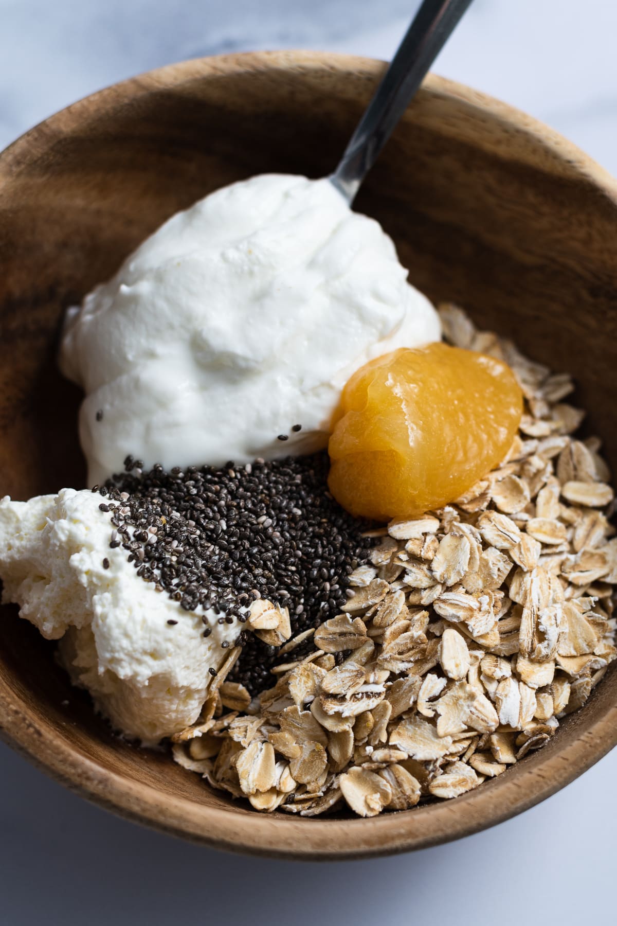small wooden bowl with rolled oats, greek yogurt, lemon curd, chia seeds, whipped cream cheese 