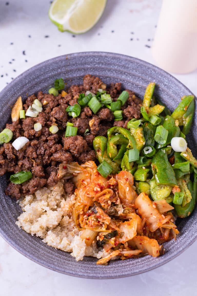 bowl with garlic ginger ground beef, fluffy quinoa, kimchi, smashed cucumber salad, sriracha mayo and sesame seeds