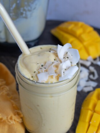 mason jar with a mango protein smoothie topped with coconut flakes and hemp hearts
