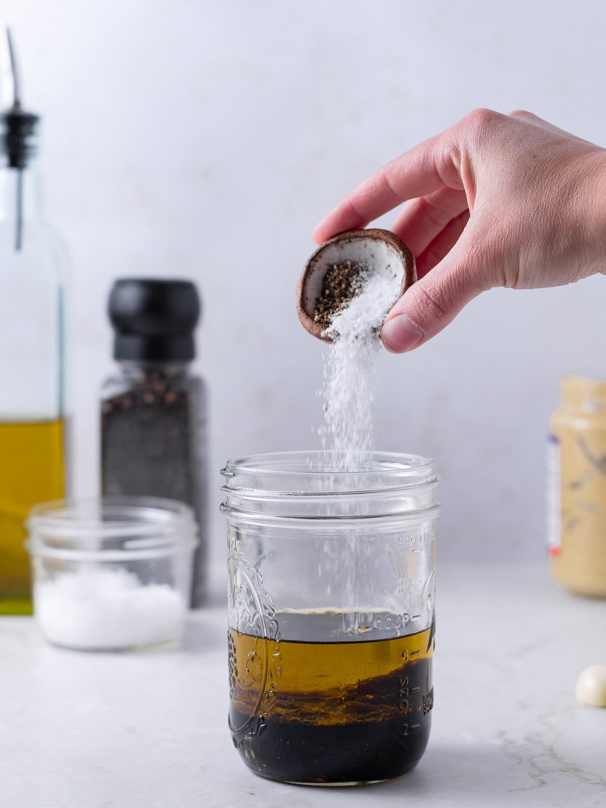 adding salt and pepper to the jar of dressing ingredients