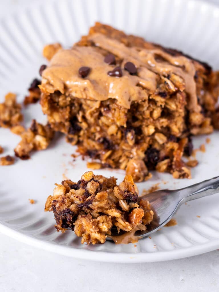 Close-up of peanut butter baked oatmeal with chocolate chips and a drizzle of peanut butter, served on a plate with a forkful in front.