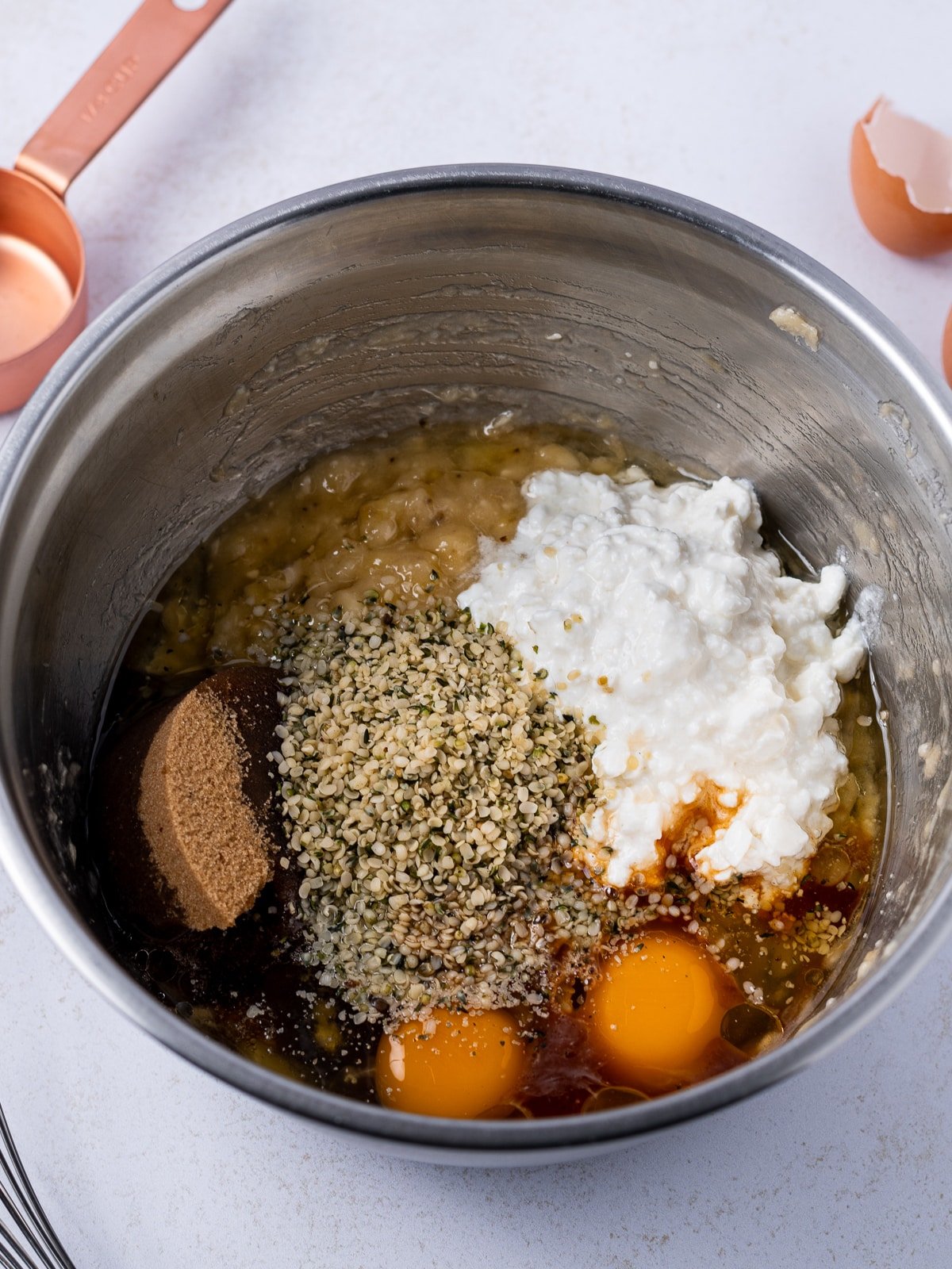 stainless steel bowl with the wet ingredients- mashed banana, brown sugar, cottage cheese, eggs, vanilla, hemp hearts