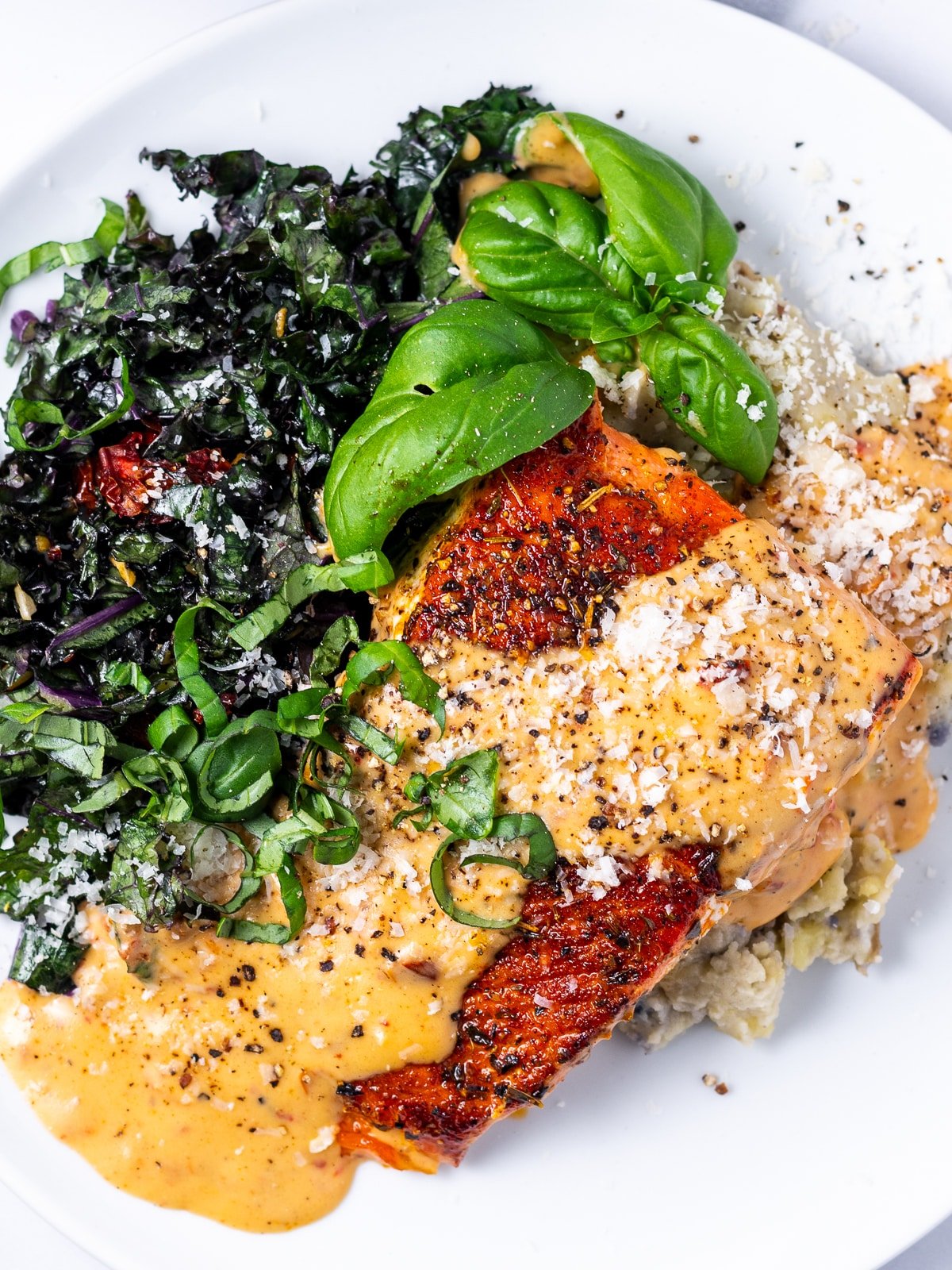 close up view of a seasoned salmon fillet with creamy sun-dried tomato sauce, parmesan cheese and fresh basil