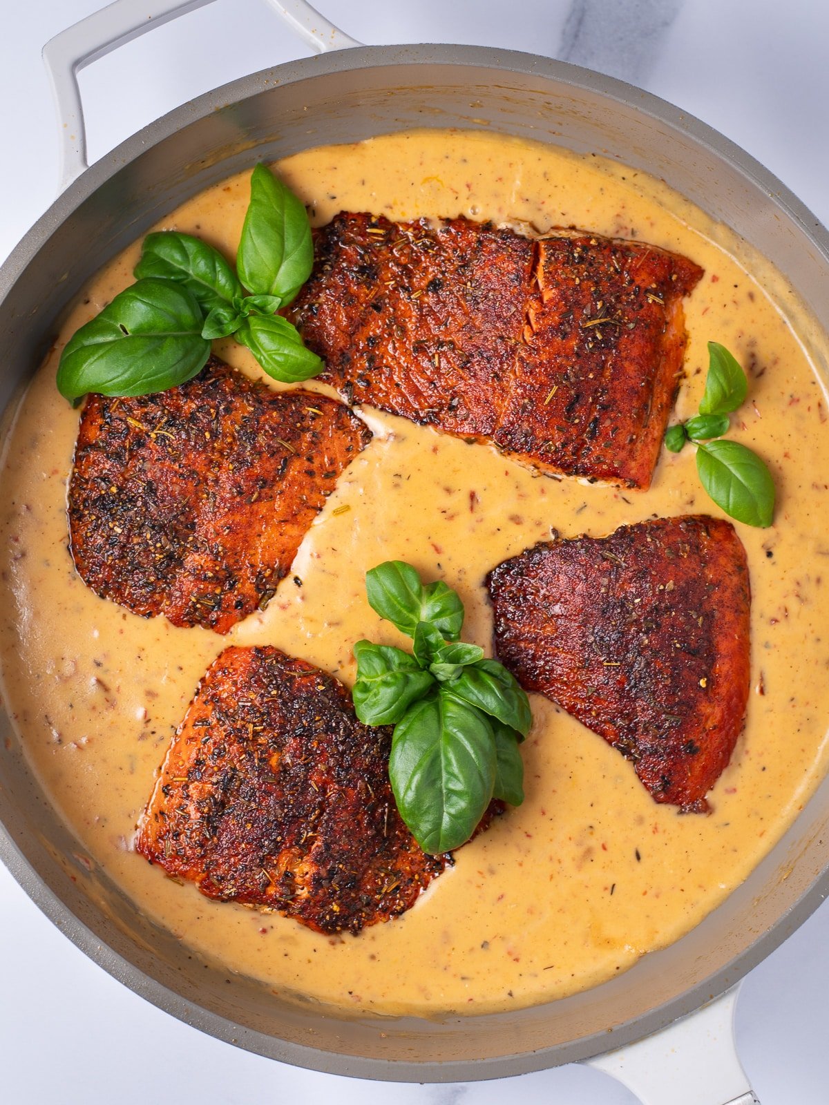 skillet with creamy sauce and four salmon fillets
