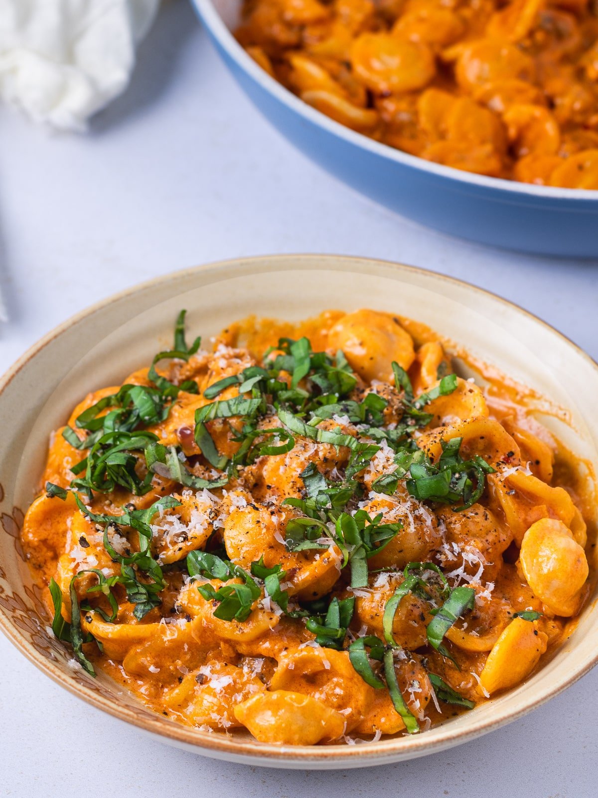 small bowl with orecchiette pasta, creamy vodka sauce and italian sausage, topped with parmesan, basil and black pepper