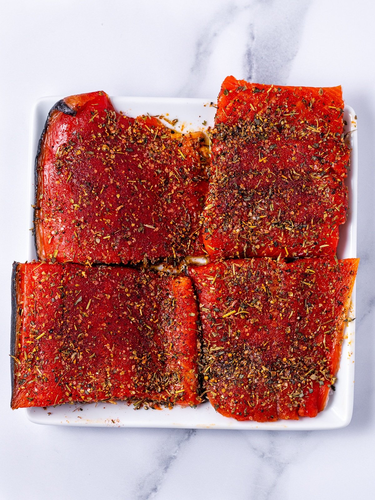 white plate with four seasoned salmon fillets