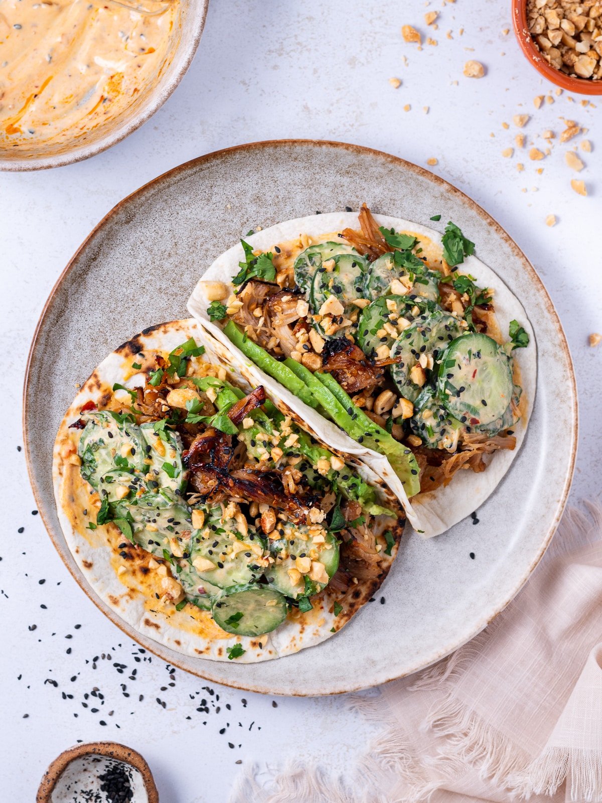 teriyaki chicken tacos on a plate topped with cucumbers and chopped peanuts