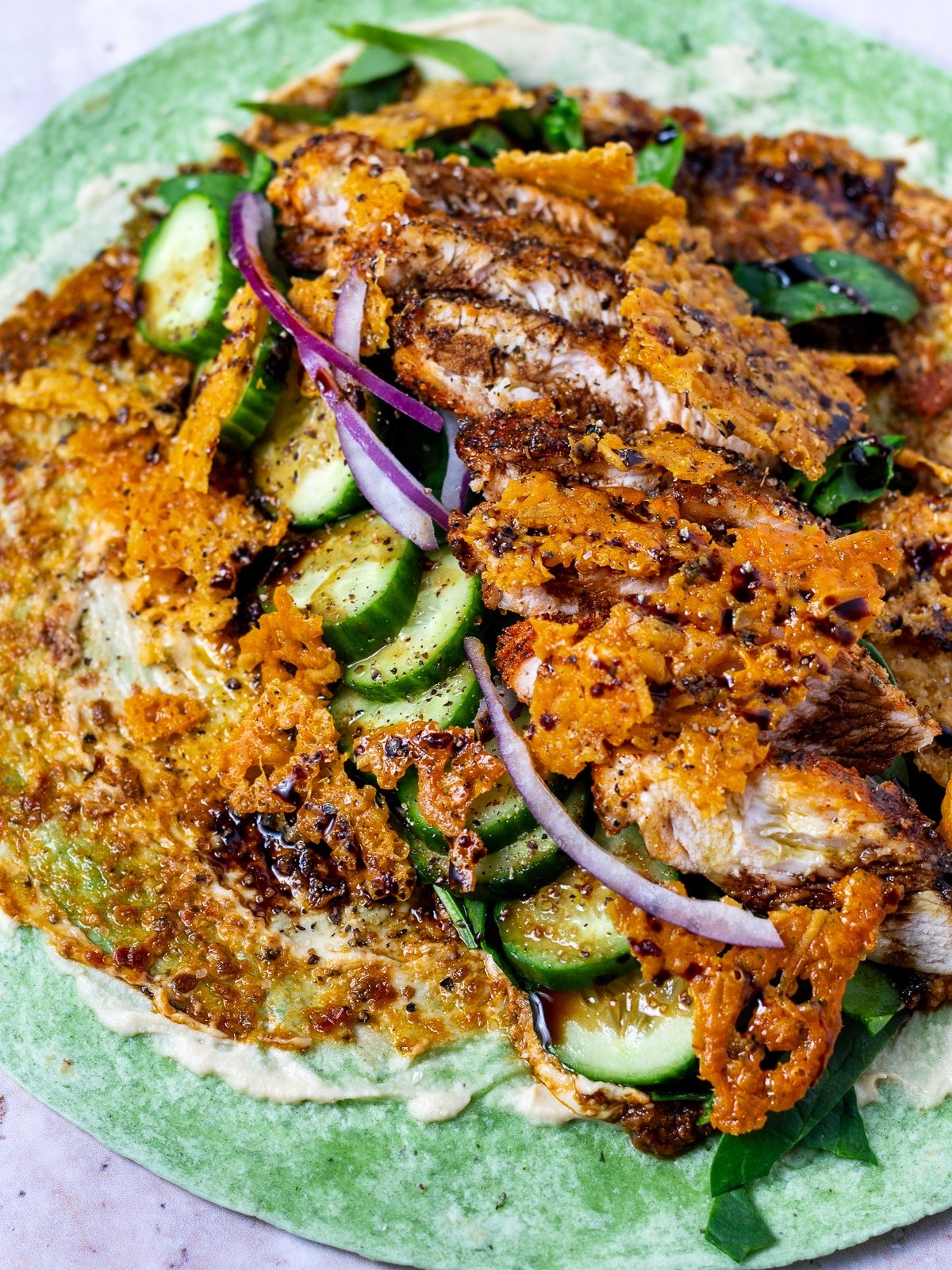 garden spinach herb tortilla spread with hummus, sun-dried tomato pesto, spinach, cucumbers, red onion, seasoned chicken and crispy parmesan