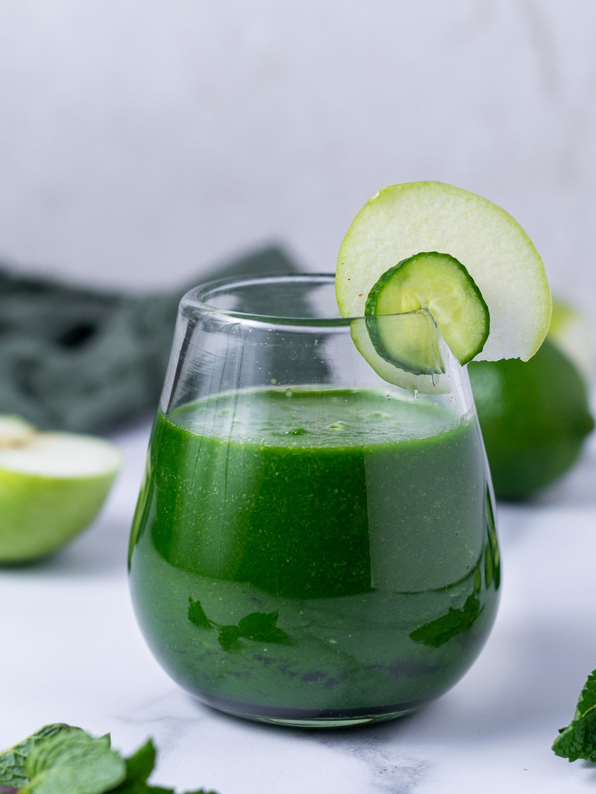 short wine glass with bright green smoothie garnished with a slice of cucumber and slice of apple