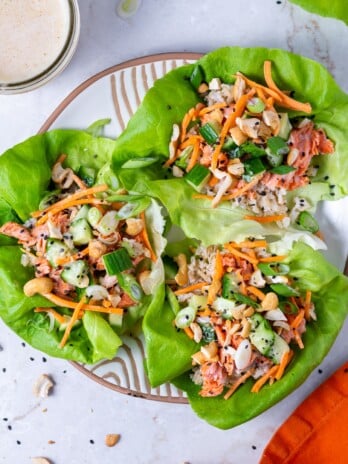 three butter lettuce leaves with salmon, cucumber, carrot, green onions, cashews and honey ginger dressing