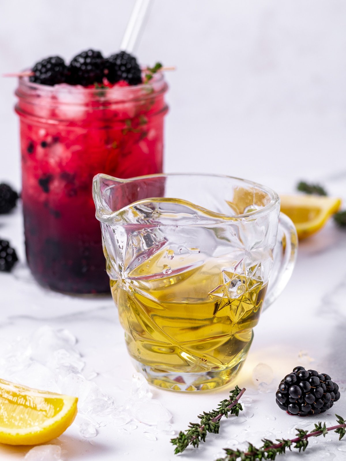 small glass of thyme simple syrup, lemon wedges, thyme sprigs and a blackberry mocktail in a mason jar