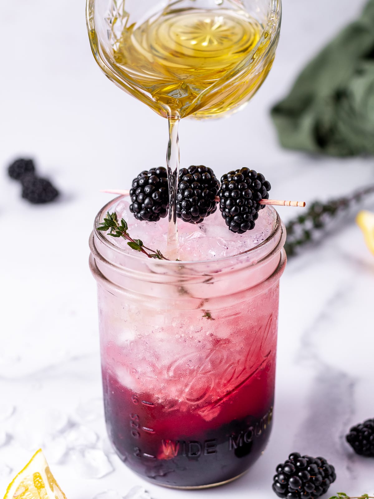 pitcher of thyme simple syrup being poured into a fizzy blackberry mocktail