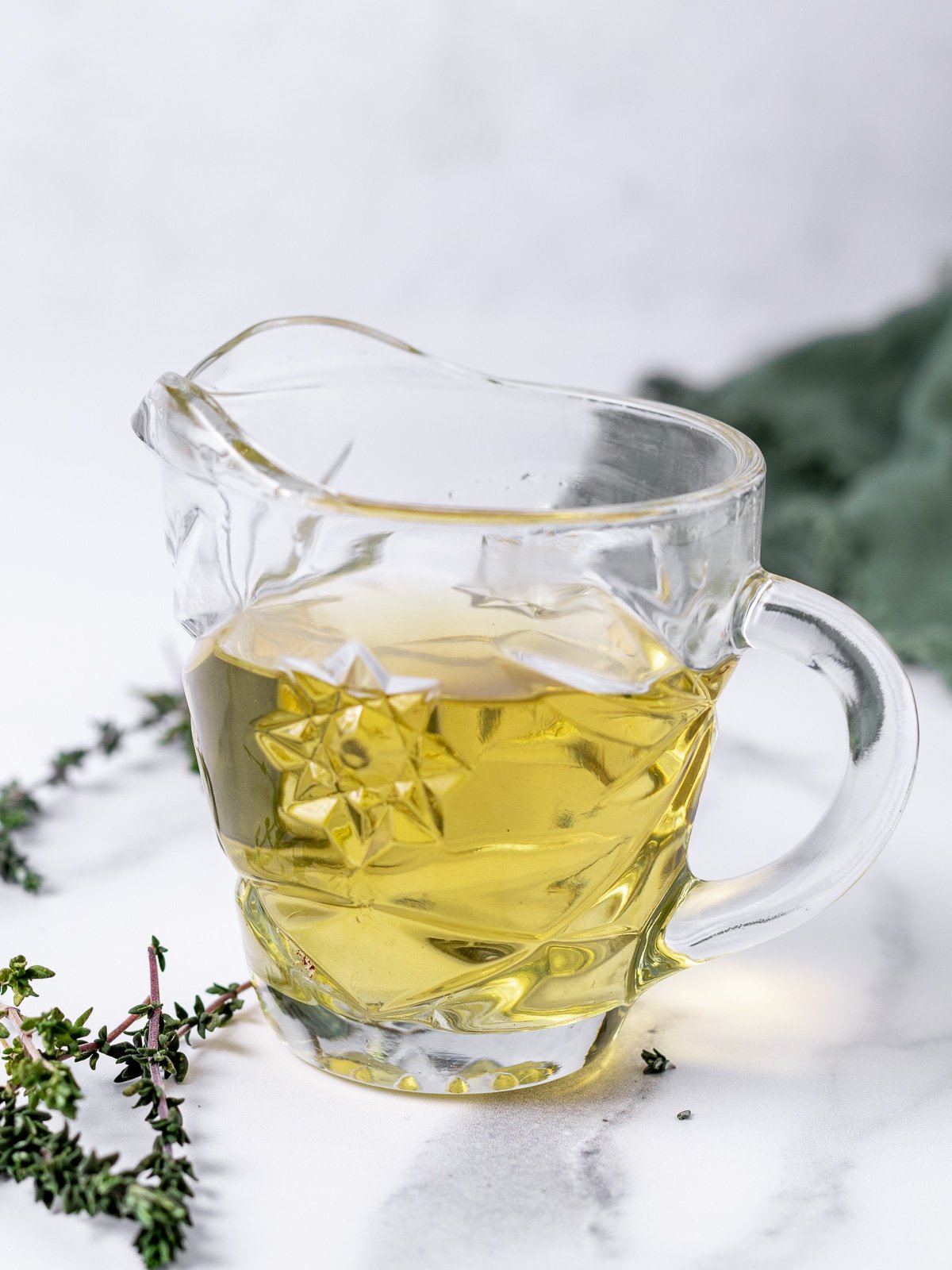 small glass pitcher of thyme simple syrup and a few sprigs of fresh thyme