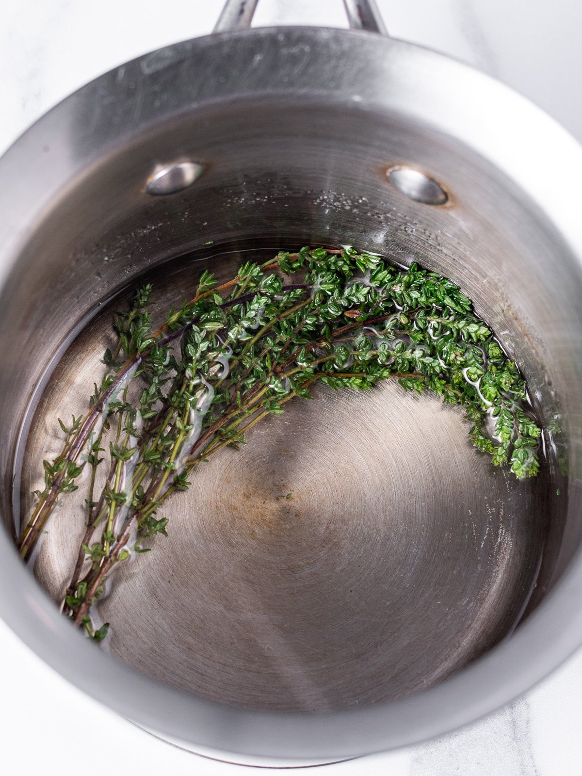saucepan with sugar dissolving into water and fresh thyme sprigs