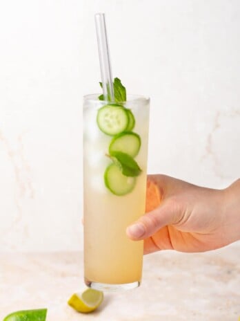 hand holding a tall glass with a coconut water mocktail garnished with mint and cucumbers