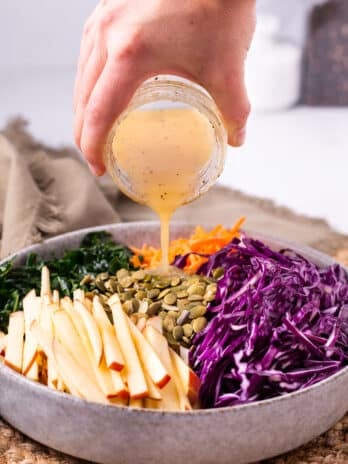 hand pouring vinaigrette on a kale and apple salad