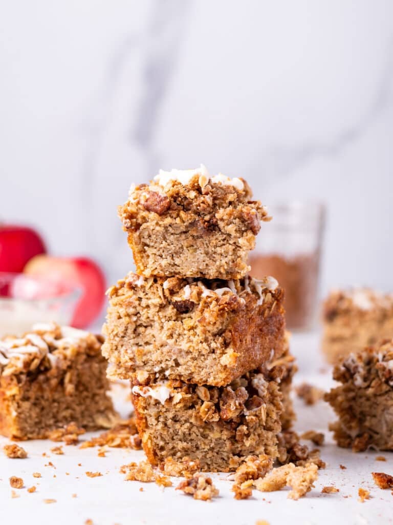 Stack of oatmeal apple cake squares with crumbly streusel topping, with fresh apples in the background.