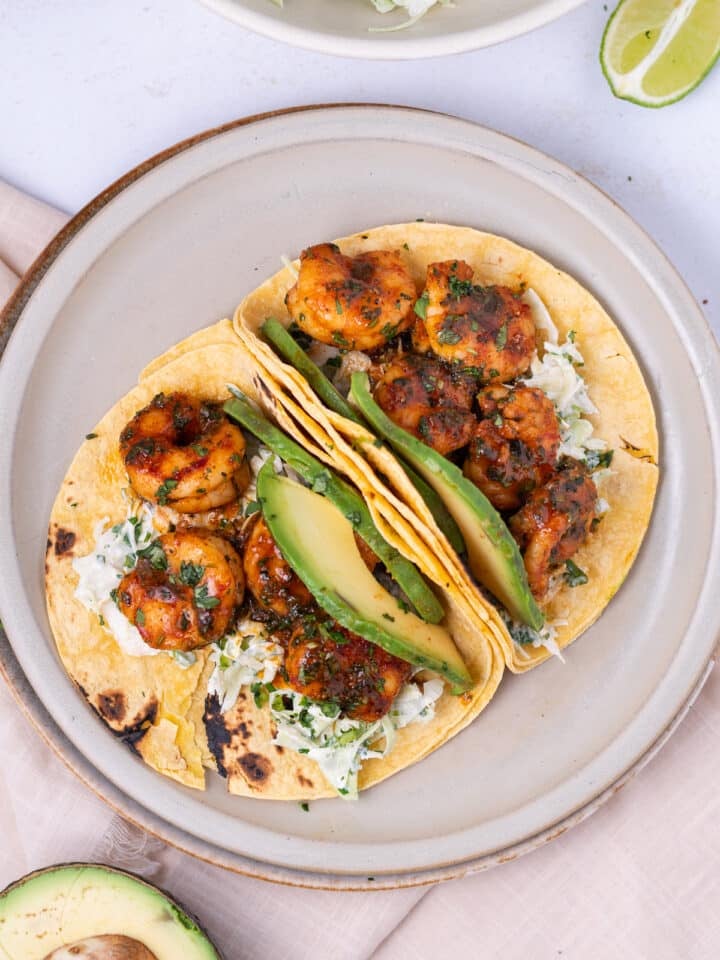 overhead view of two tacos filled with cabbage, seasoned cilantro lime shrimp and avocado slices