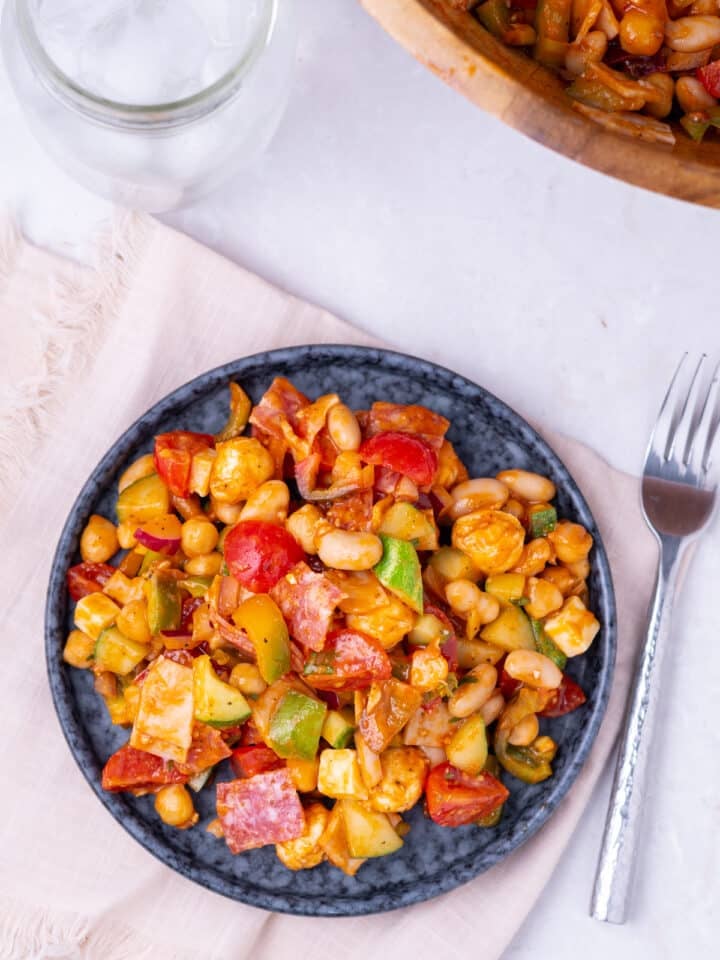 Protein-packed dense bean salad made with beans, cucumbers, peppers, and tomatoes served on a plate.