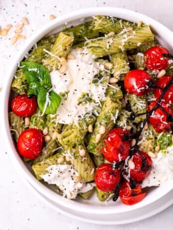 white bowl with pesto pasta, burst tomatoes and burrata cheese