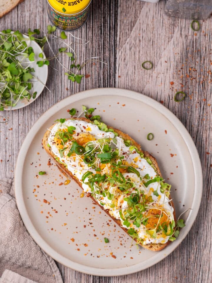beige plate with sourdough toast, avocado, cottage cheese, egg, microgreens and green onions