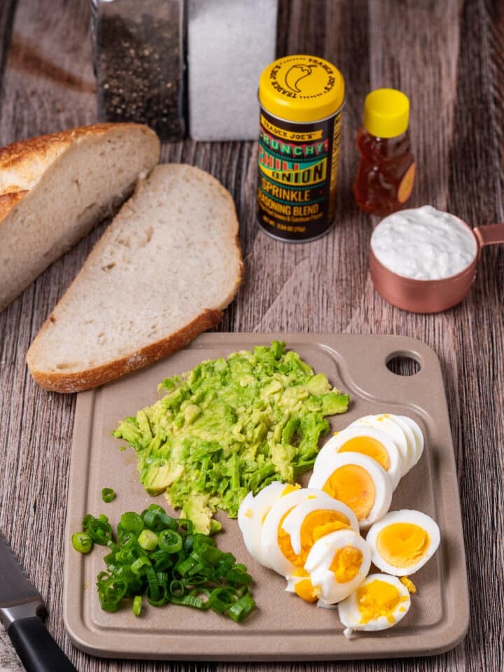 small cutting board with sliced egg, smashed avocado, chopped green onions and a loaf of sourdough bread