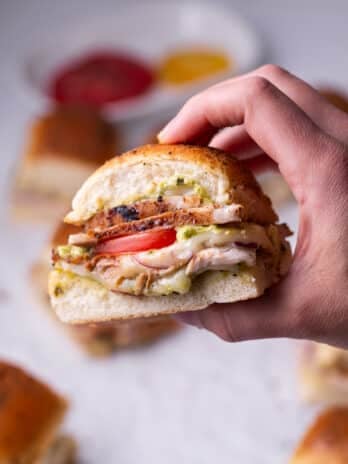 hand holding a slider with chicken, pesto mayo, tomato, red onion and mozzarella cheese