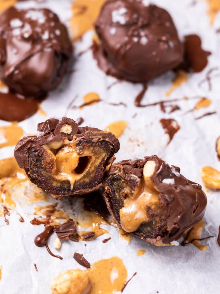 Chocolate-covered dates cut open to show the peanut butter and peanut filling inside.