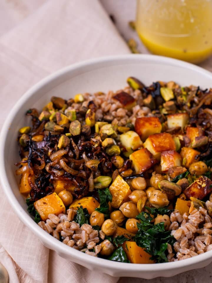 close up view of a farro grain bowl with cooked farro, crispy chickpeas, fried shallots, bread cheese and pistachios