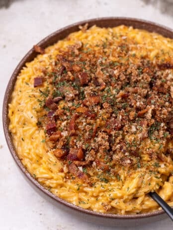 large bowl with cheesy orzo topped with bacon breadcrumbs and dried parsley
