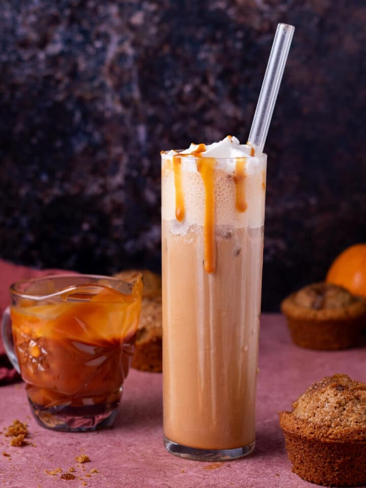 tall glass with iced salted caramel latte, small pitcher of salted caramel syrup and pumpkin muffins