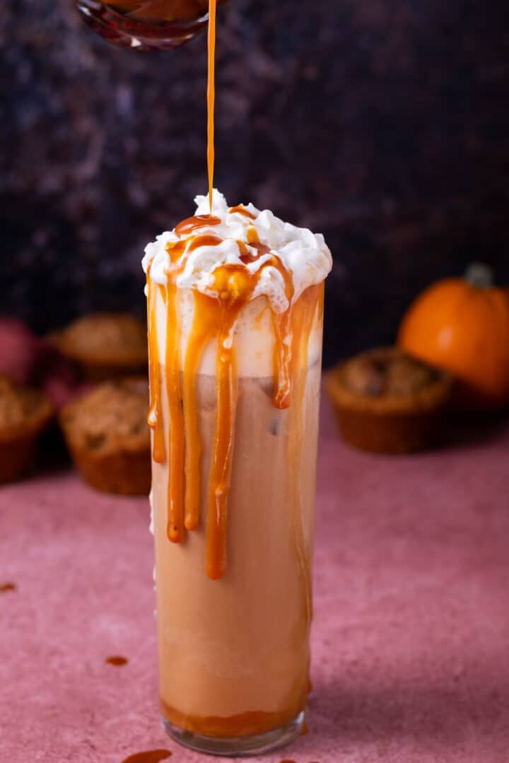 pouring caramel syrup on an iced latte topped with whipped cream