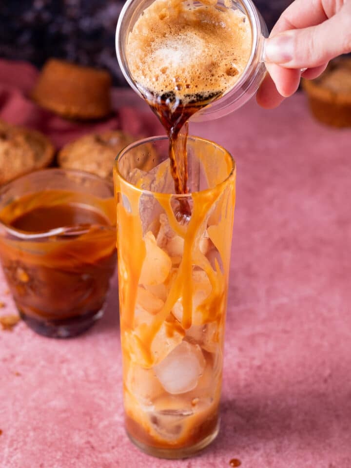 hand pouring espresso shot into a glass drizzled with salted caramel syrup