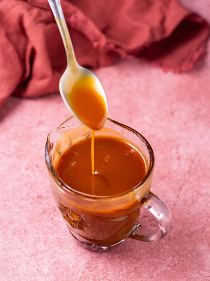 Spoon drizzling salted caramel into a small pitcher of caramel syrup