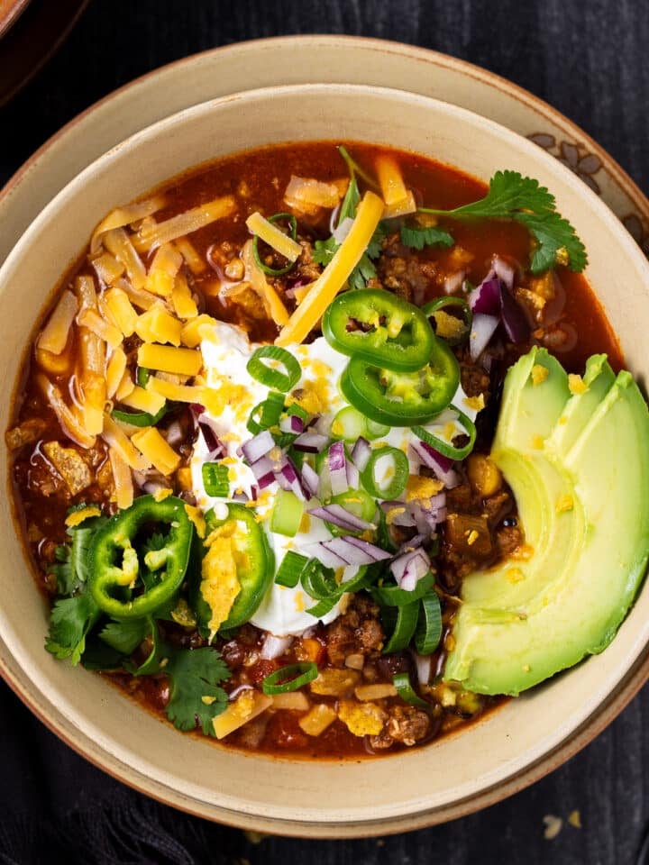 Bowl of taco soup topped with shredded cheese, avocado, jalapeño, red onion, herbs and Greek yogurt.