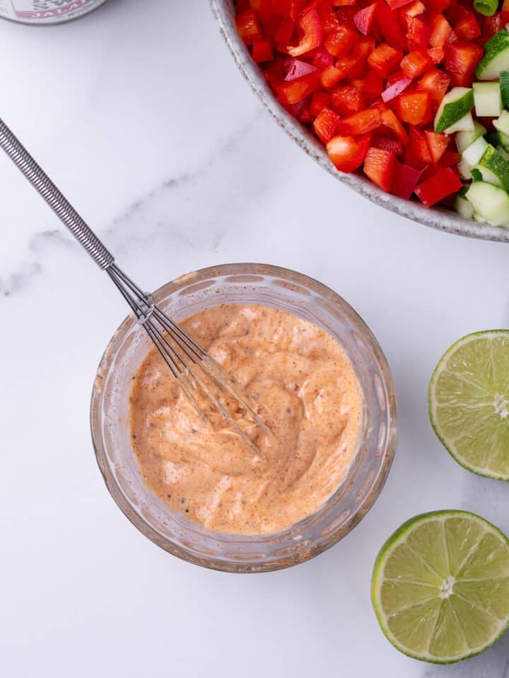 small glass bowl with whisked together creamy dressing, small whisk in the mixture