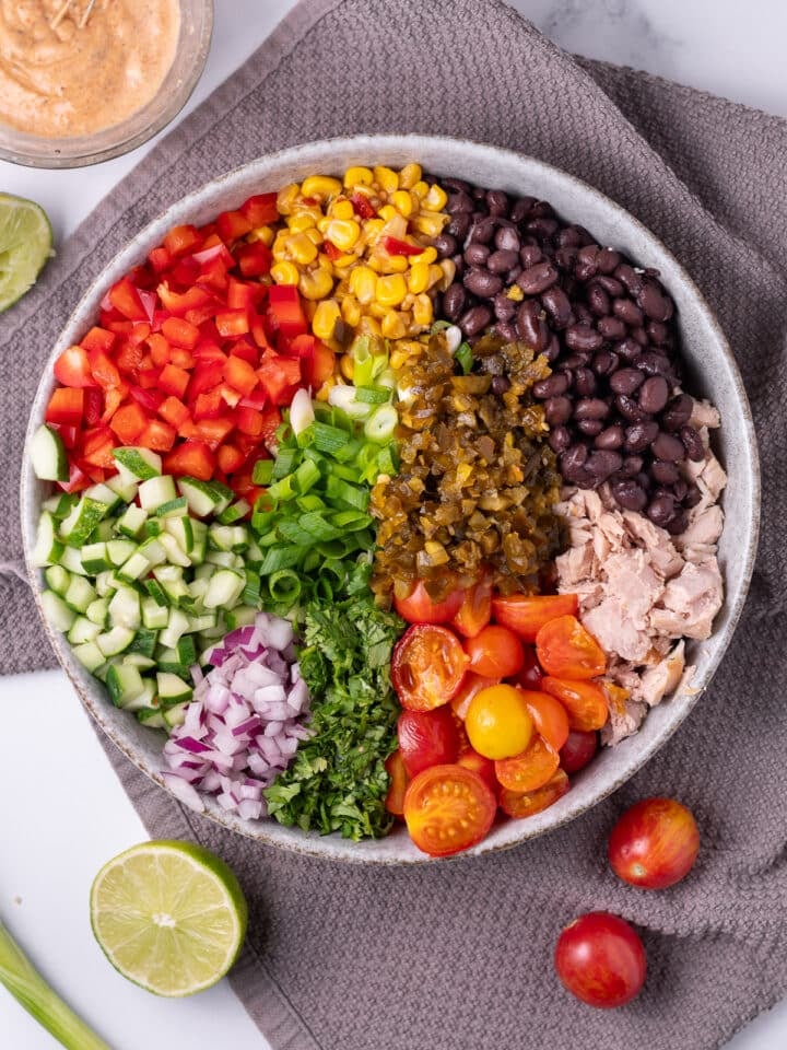 large salad bowl with red bell pepper, corn salsa, black beans, tuna, tomatoes, cilantro, green onions, red onion and cucumber