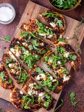 large wooden cutting board with caramelized onion flatbread topped with goat cheese, arugula and balsamic glaze