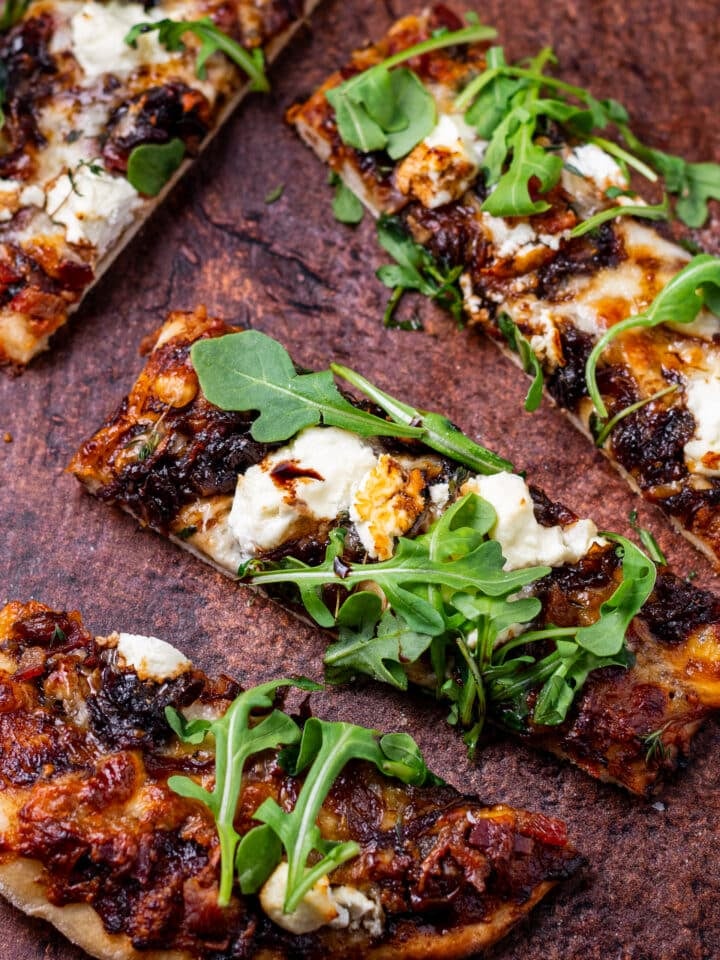 close up view of a slice of caramelized onion flatbread with goat cheese, balsamic glaze and arugula