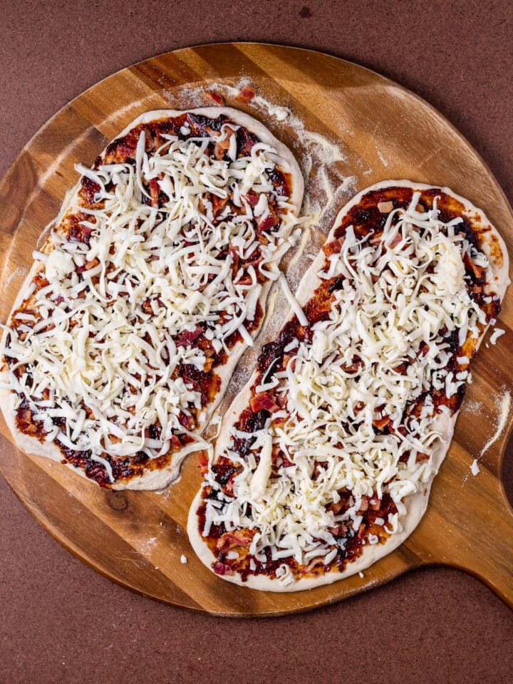 gruyere cheese added to pizzas on a pizza peel