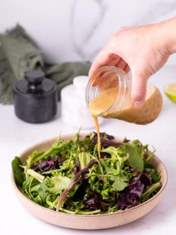 hand pouring a jar of ginger lime dressing on mixed greens