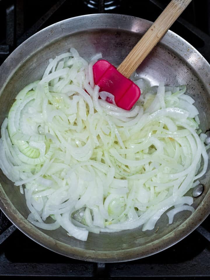 sliced onions tossed with butter and oil, red spatula