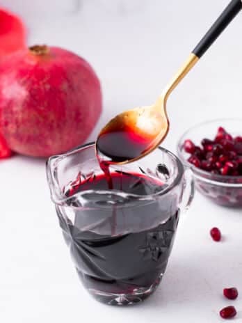 gold spoon drizzling a spoonful of pomegranate syrup into a small pitcher