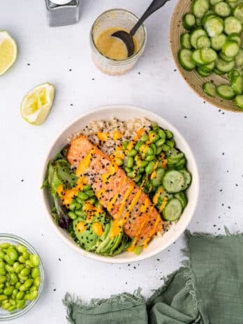 white bowl with cucumber, edamame, salmon fillet, ginger lime dressing and mixed greens